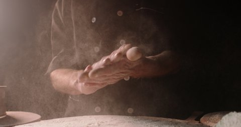 Experienced professional chef getting rid of flour on his hands, starting to make pizza or bread dough at bakery, isolated on black background close up 4k footage