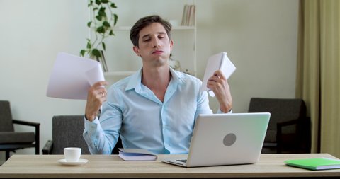 Businessman suffering from summer heat in office home, sitting in stuffy room. Annoyed jaded worker man uses notebooks to freshen himself up with paper documents, air conditioning problems.