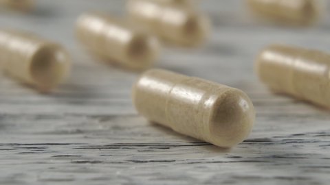 Beige herbal medical capsules on a wooden light background. Macro dolly shot. Selective focus