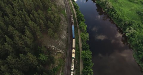 Freight long train carries with cargo carriages in a village in wild mountains landscape through a difficult part of Trans Siberian railways. Aerial drone wide view at summer day.