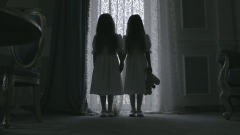 Creepy twin girl silhouettes standing in mysterious dark haunted room, thriller