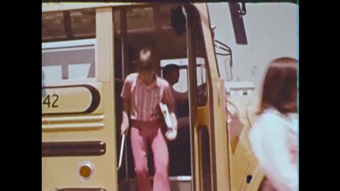 CIRCA 1970s - American Junior High School students exit a school bus, and their teacher quizzes them on school bus protocol in the 1970s.