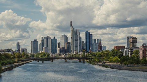 Frankfurt skyline time lapse, blue sky with clouds, office buildings and skyscraper in center with river and bridges in the foreground
