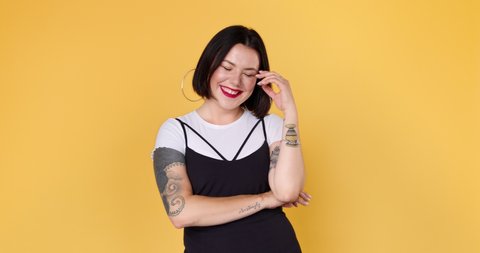 A young embarrassed woman with tattoo is listening compliments shy and laughing in yellow studio isolated. Portrait of shame female embarrassed smile. Shyness person expression.