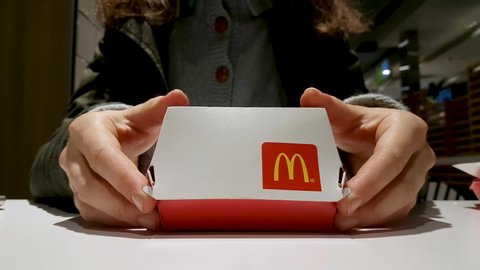 Big Mac box with McDonald's restaurant logo. Hands open box with Big Mac, woman picks up burger and eats. Minsk, Belarus - August 8, 2020.