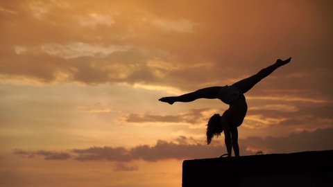 Flexible girl doing handstand on sky background during dramatic sunset in slow motion 