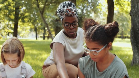 African-American female teacher helping girl with exercise in workbook during outdoor lesson in the park
