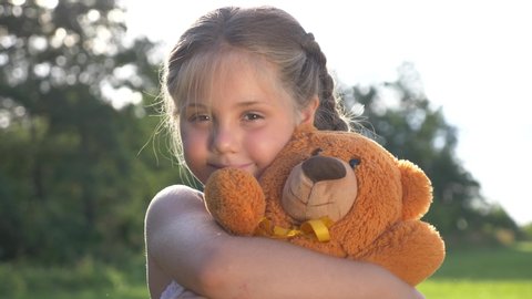 A little girl hugs her favorite toy. A child plays with a Teddy bear. A soft toy in the hands of a baby. A happy kid plays in the Park with a toy and dreams.
