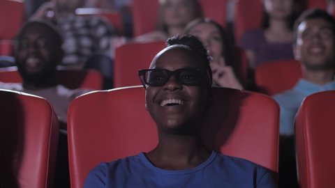 Close-up portrait of cheerful african american female watching exciting 3d movie expressing delight with wow exclamation. Excitement and wide smile on face of emotional dark-skinned woman in cinema