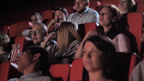 Cheerful groups, couples of audience enjoying free time in movie theater. Joyful spectators chatting, relaxing, eating popcorn, drinking soda while watching film in cinema hall