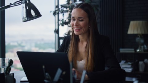 Smiling businesswoman using laptop computer for work in office. Positive female professional reading document at laptop screen indoors. Portrait of happy business woman typing on laptop keyboard