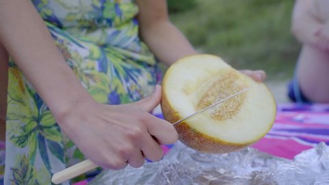 Close up on hands of unknown caucasian woman cutting melon in summer day with knife on the field prepare fresh organic raw food on picnic 