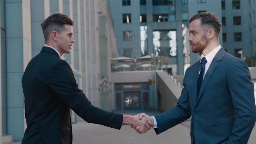 Two business partner shake hands when meeting. Portrait of handshake of two successful businessmen making a deal. Office building on the background. Business district.