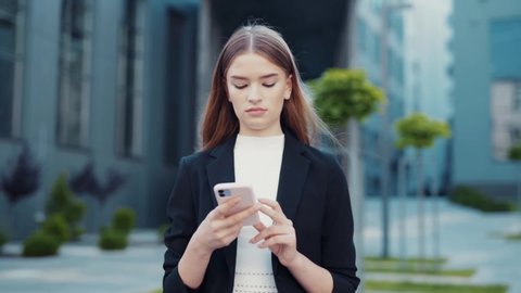 Adult Caucasian Confident Young Business Woman in White Shirt is Talking on Phone Outside near Modern Office Building. Medium Long Low Angle 4K Slow Motion Corporate Shot with Moving Around 360 Camera