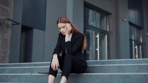 Unhappy european young fired woman sits on the stairs and frustrating feeling sad of losing prestigious job. Unemployment. Job crisis. Broken ambitions.