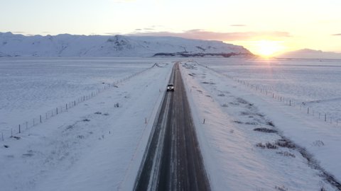 Wide Shot of Jeep Car driving on Iceland Road with Snow white Mountains and Sunset countryside, Winter, Aerial tracking dolly backwards