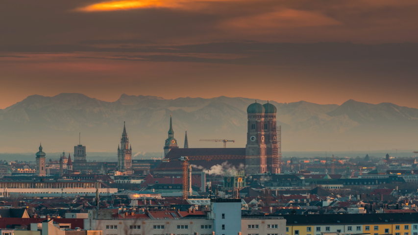 Munich skyline sunset over old town downtown in front of most poular church in city. In background alps mountains, munich germany panoramic view at sunset time lapse from day to night. Munich downtown Royalty-Free Stock Footage #1057692892