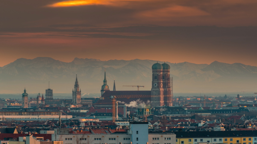Munich skyline sunset over old town downtown in front of most poular church in city. In background alps mountains, munich germany panoramic view at sunset time lapse from day to night. Munich downtown