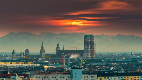 Munich skyline sunset over old town downtown in front of most poular church in city. In background alps mountains, munich germany panoramic view at sunset time lapse from day to night. Munich downtown