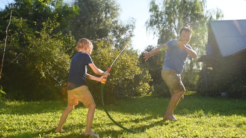 Funny little boy with his father playing with garden hose in sunny backyard. Preschooler child having fun with spray of water. Summer outdoor activity for family with kids. Royalty-Free Stock Footage #1057693120