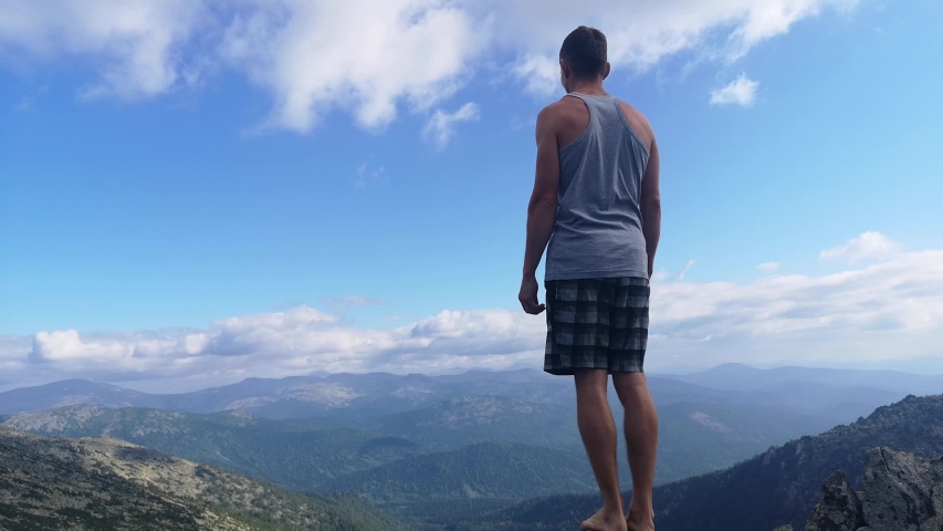 man stands on top of a mountain with open hands.
