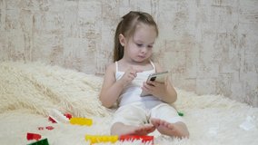 A child plays on the phone while sitting on the couch with the designer. Toy in the smartphone. Life as a distance preschool education. Modern baby.
