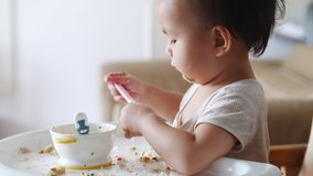 Side view close up 60 fps 4k video of little asian baby eating lunch by herself adorable Chinese baby girl learning to feed herself baby eating playing with the spoon