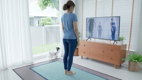 Back view : asian woman stretching body and yoga in living room at home with pet, watching live or video tutorial TV online. Activity during quarantine and social distance new normal concept.