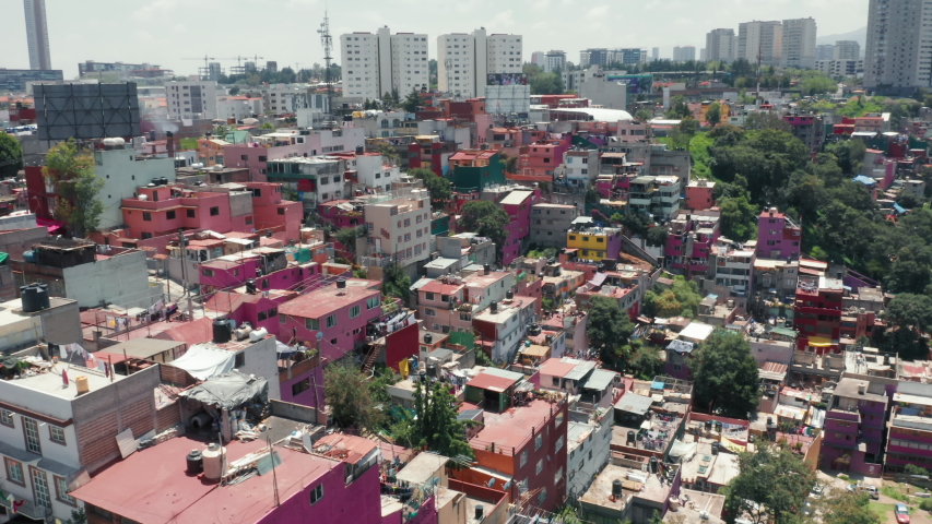 Traveling Central America, exploring Mexico city. Pink low-income slum building in Mexico suburban. Vibrant favelas with Mexico city skyline on background. Colorful favelas in latin area. 4K aerial Royalty-Free Stock Footage #1057700146