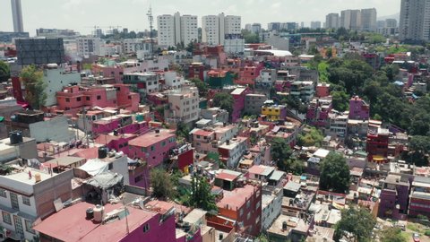 Traveling Central America, exploring Mexico city. Pink low-income slum building in Mexico suburban. Vibrant favelas with Mexico city skyline on background. Colorful favelas in latin area. 4K aerial