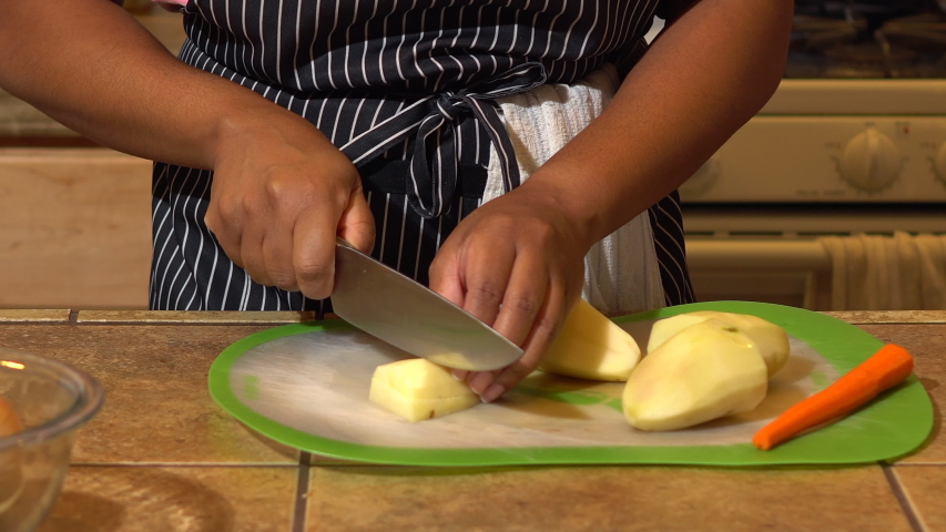 Black woman slicing potatoes on silicone cutting board in kitchen, CLOSEUP