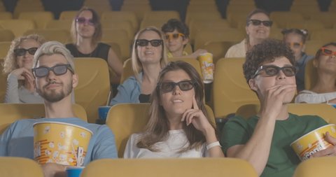 Engrossed people watching 3d film in cinema as unrecognizable man passing at front. Portrait of irritated visitors distracted from premiere in movie theatre. Angered audience. Cinema 4k ProRes HQ.
