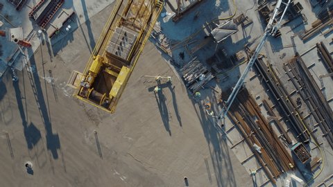 Aerial Flight Over a New Constructions Development Site with High Tower Cranes Building Real Estate. Heavy Machinery and Construction Workers are Employed. Top Down View at Contractors in Safety Hats.