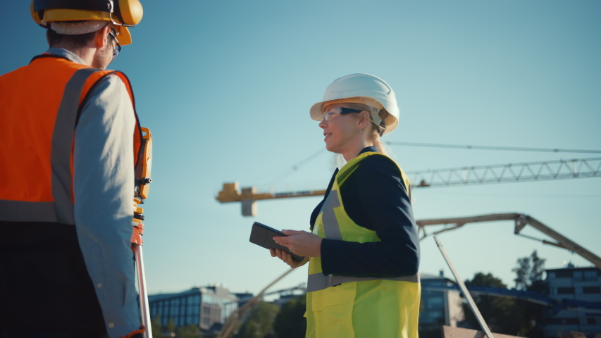 Construction Worker Using Theodolite Surveying Optical Instrument for Measuring Angles in Horizontal and Vertical Planes on Construction Site. Engineer and Architect Using Tablet Next to Surveyor. Royalty-Free Stock Footage #1057704850