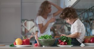Portrait of young parents arguing at the kitchen while their son is sitting next to them and looking at them. Also, in the foreground are different vegetables and fruits as a decoration. 4K video