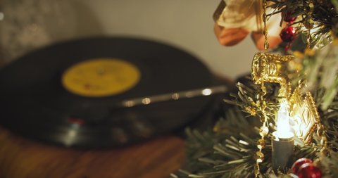 Record spins on a turntable in the background of a small decorated Christmas tree with glowing lamps on Christmas Eve.