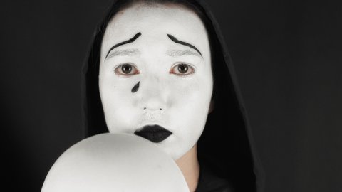 Brunette puts on a white theater mask. Theatrical makeup sad mask. The woman hides emotions behind a mask of indifference.