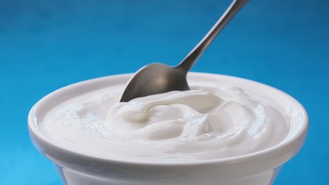 Bowl of sour cream on blue background, greek yogurt with spoon