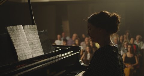 4K Footage Of Female Pianist Plays In Beautiful Grand Piano On Stage In Concert . A woman plays the piano in the concert hall . Many unrecognizable , blurred people in the background . 