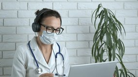 Doctor consult by computer. A doctor in uniform and medical mask speak on webcam on internet.