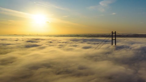 Aerial reveal of the Humber Bridge as the sun is rising with low cloud and fog passing by very quickly