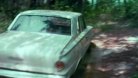 CIRCA 1973 - In this classic crime movie, a robber on the run from the law drives through the woods and over a cliff.
