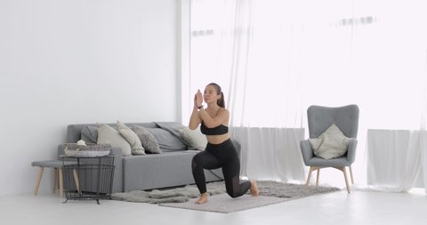 Girl is having workout. Athletic young woman is training and doing lunges in jump at home in living room. She does fitness physical exercise. Workout, sport, fitness, training and wellness concept.