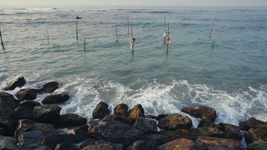 Waves Splashing On The Rocky Coast With Wooden Stilts Planted On The Ocean In Weligama, Matara, Sri Lanka. -wide shot