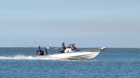 PORT ARANSAS, TX - 7 FEB 2020: Fishing boat with outboard motor and three people, slowing down as they enter the marina on a sunny day, floating past rocks and birds on breakwater,