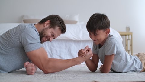 Family fitness at home, Father coach, Sports kid, Fun gymnastics. Cheerful dad and son are fighting with their hands while lying on the floor at home