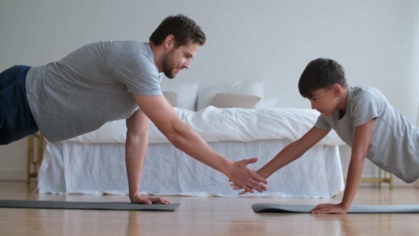 Family fitness at home, Father coach, Sports kid, Fun gymnastics. Dad and son are doing push-ups from the floor and touching their hands lying on the floor opposite each other Royalty-Free Stock Footage #1057750744