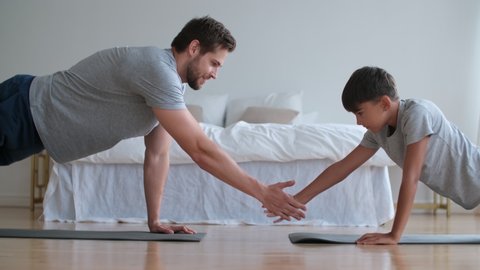 Family fitness at home, Father coach, Sports kid, Fun gymnastics. Dad and son are doing push-ups from the floor and touching their hands lying on the floor opposite each other