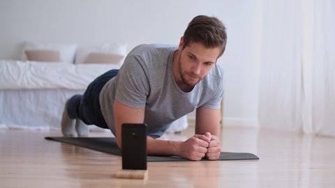 Family fitness at home, Father coach, Sports kid, Fun gymnastics. Attractive man doing sports exercise lying on the floor at home and timing the time on the smartphone