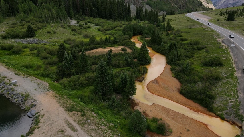Aerial view Moving forward shot, Car’s Moving along the road of Uncompahgre National Forest in Colorado, Scenic view mud covered stream and pine trees in the background.